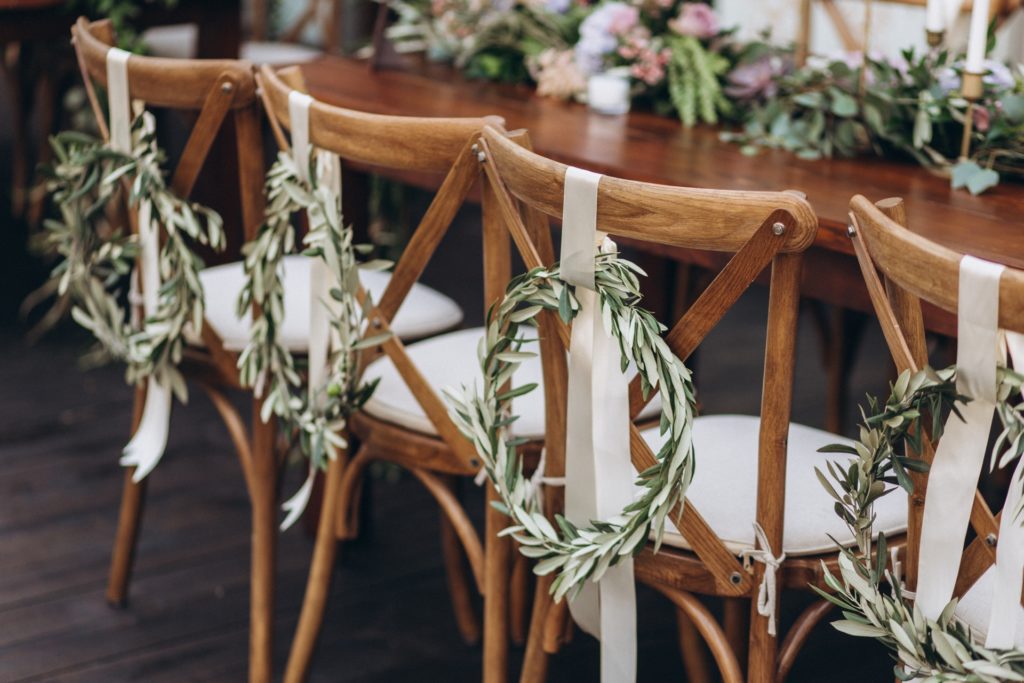 Rustic greenery wreaths on back of chairs at country wedding