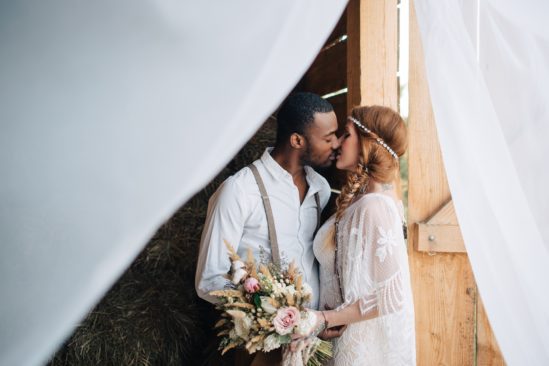 Boho bride kissing groom outside barn at country wedding