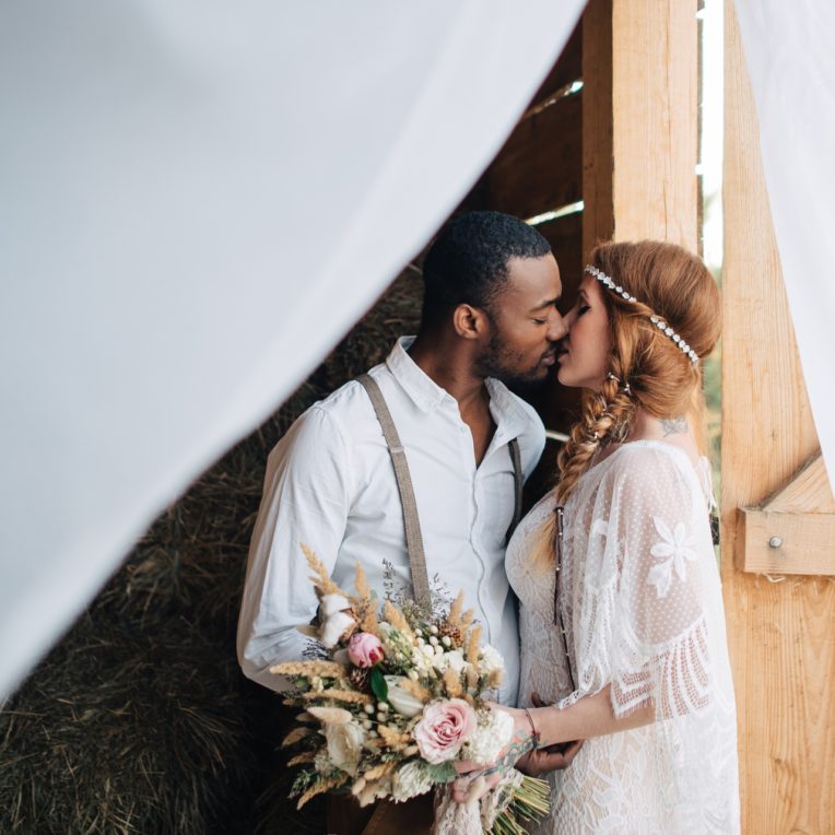 Boho bride kissing groom outside barn at country wedding