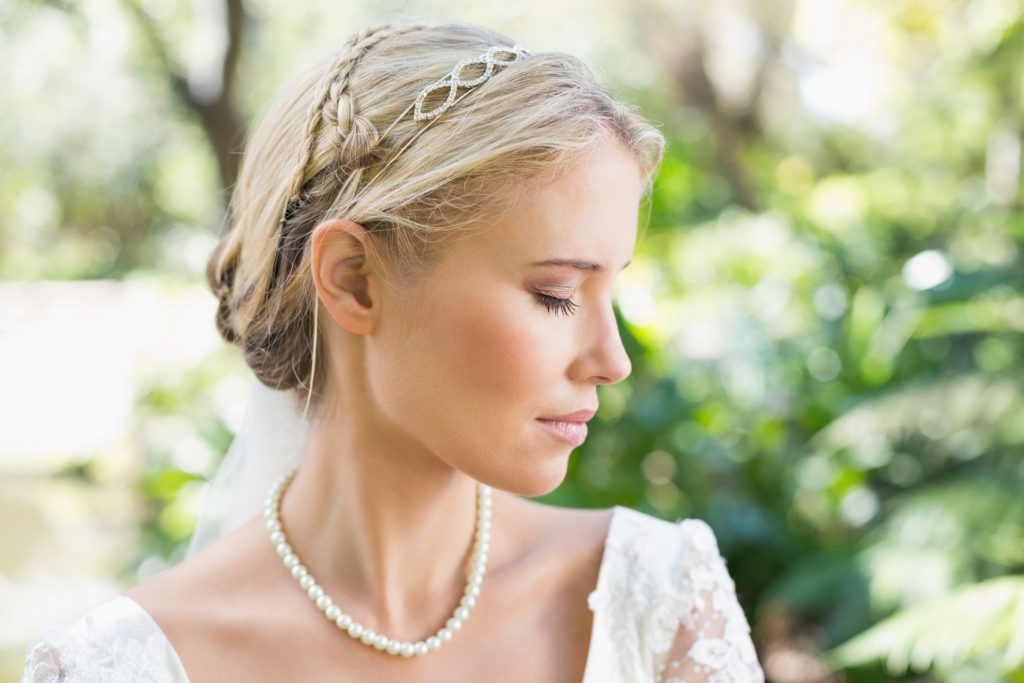Demure bride in garden posing for portrait wearing a strand of pearls