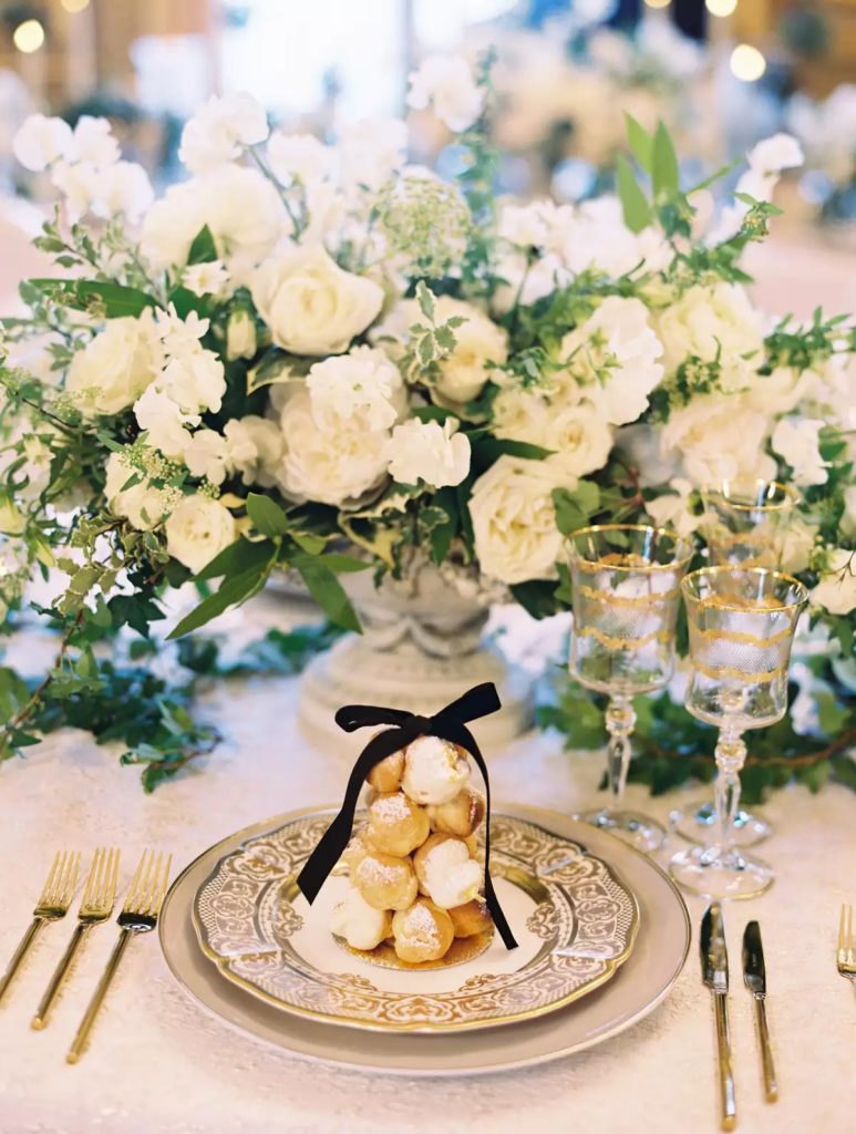 Plated croquembouche on table with flowers behind it