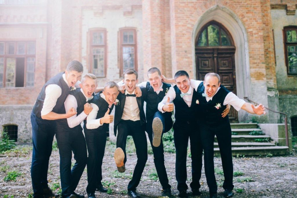 Groom kicking up shoes with arms around groomsmen celebrating wedding day