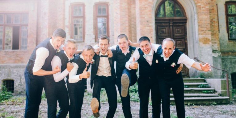 Groom kicking up shoes with arms around groomsmen celebrating wedding day