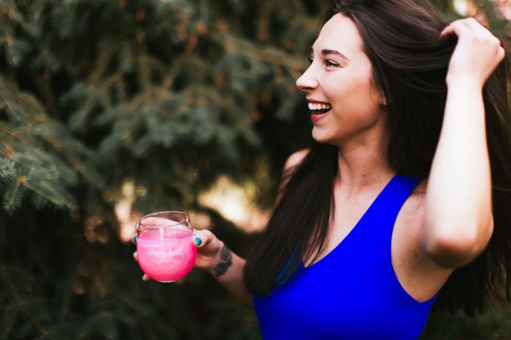 A woman in blue holding a glass of Wonderdust™ - an effervescent glitter hydration supplement