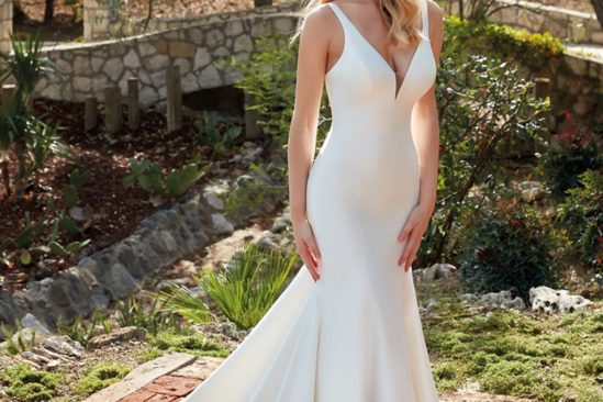 Bride with long blonde hair wearing simple V-neck wedding gown outside on brick path
