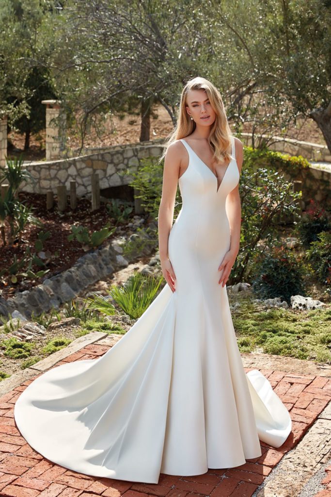 Bride with long blonde hair wearing simple V-neck wedding gown outside on brick path