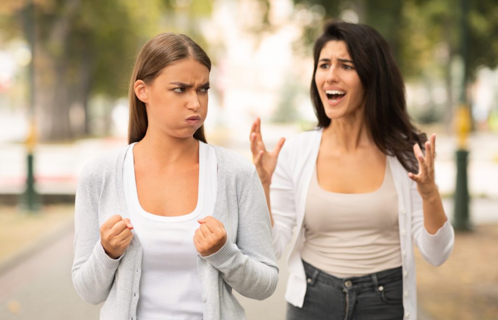 Woman clenching fists while friend yells at her while walking down street