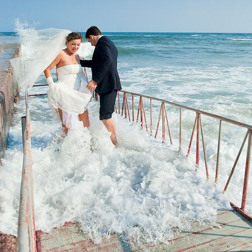 Stunning photo of bride and groom being surrounded by crashing waves while trying to capture picture