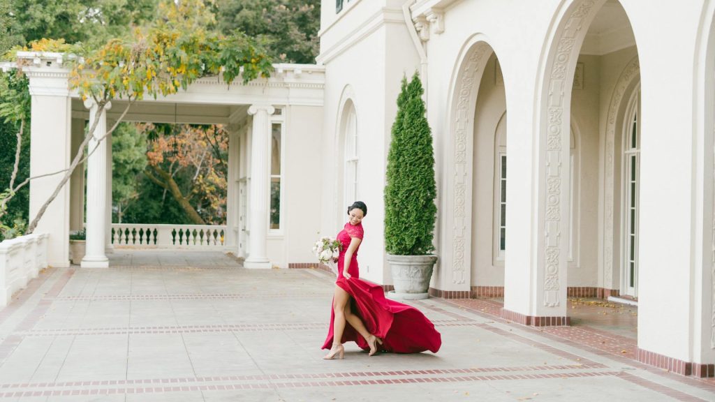 Bride walking in red wedding dress in front of large white mansion