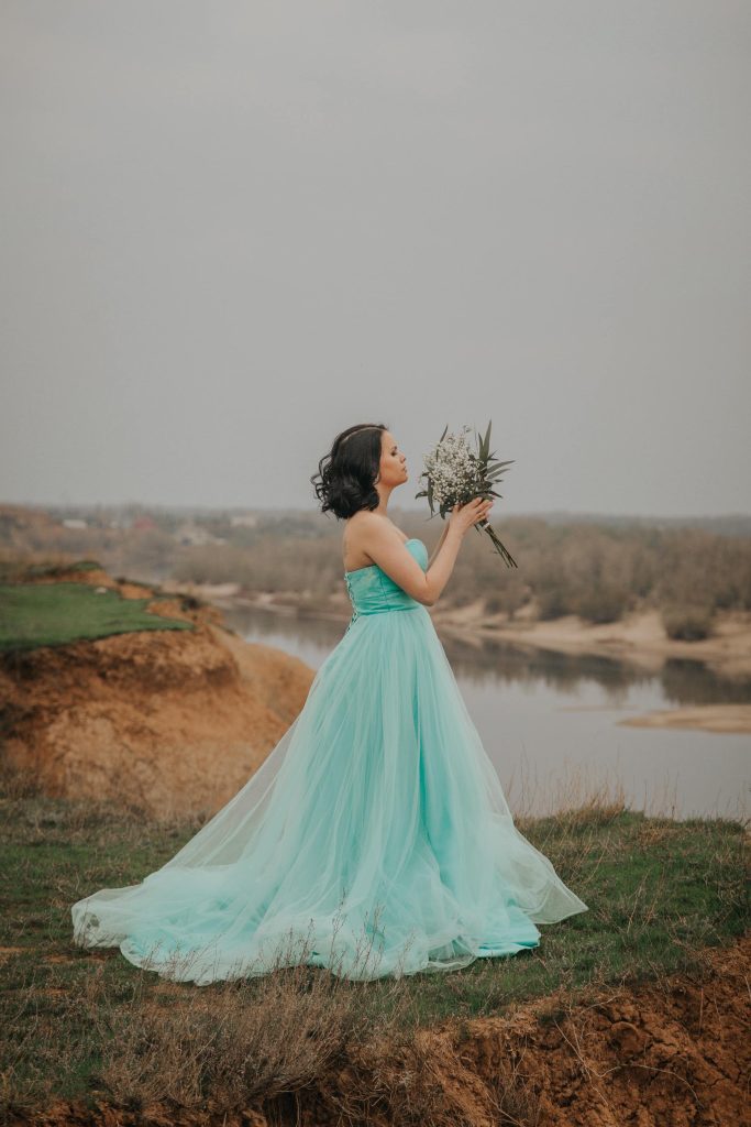 Bride in soft teal dress standing in field and holding flowers