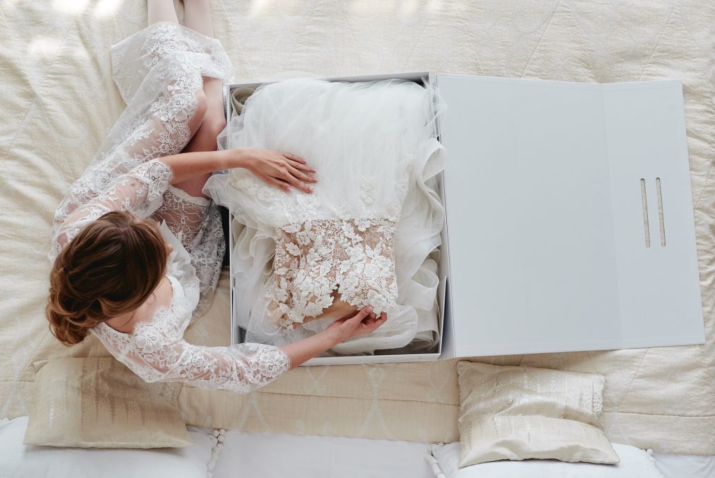 woman sitting on bed putting her wedding dress in a box