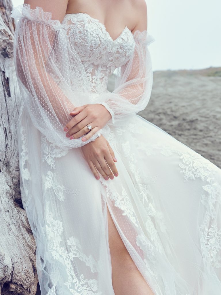 bride wearing lace wedding dress with high slit and bishop sleeves leaning against a tree