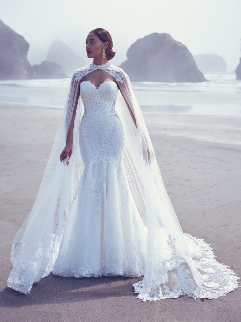 beautiful bride on the beach wearing fitted lace wedding dress and dramatic wedding cape by Maggie Sottero