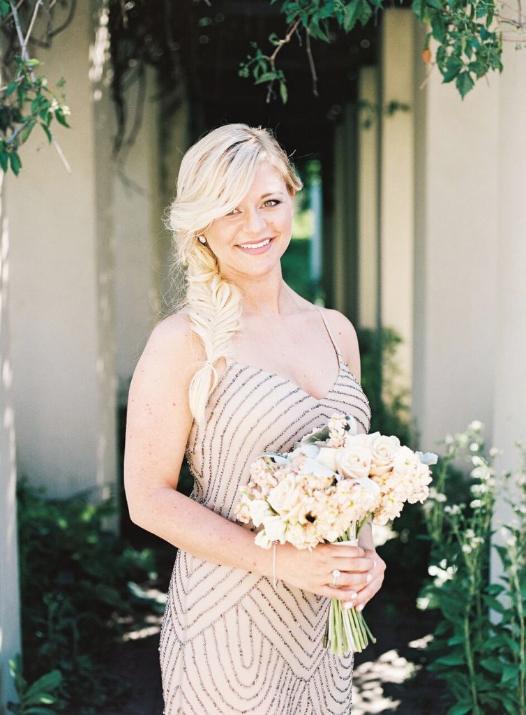 Blonde bridesmaid poses outside with bouquet.